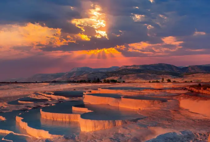 The white travertine terraces of Pamukkale lit copper by a low sunset.